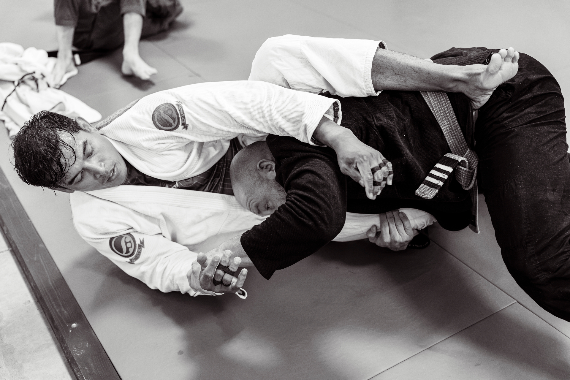 Two Brazilian Jiu-Jitsu athletes grappling on the mat under moody light